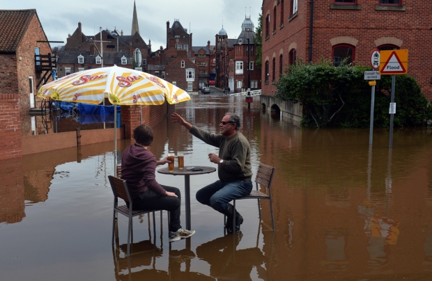 Ανδρες κάθονται στα νερά των πλημμυρών έξω από ένα μπαρ, καθώς τα επίπεδα του νερού συνεχίζουν να αυξάνονται στις όχθες του ποταμού Ouse στο York, βόρεια Αγγλία,